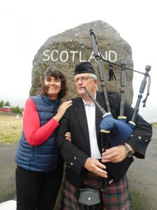 Carleeta and a bagpipe player in front of a huge rock with Scotland painted on it.