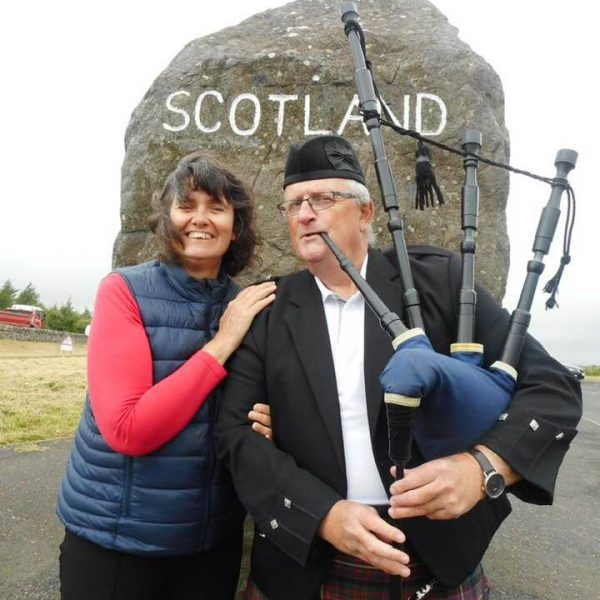 Carleeta and a bagpipe player in front of a huge rock with Scotland painted on it. 