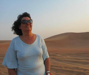Carleeta smiling - it is dusk in the desert. Sandunes are behind her.