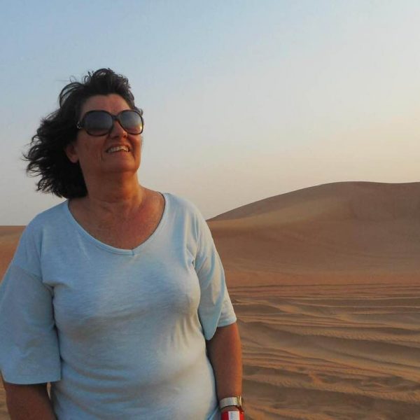 Carleeta smiling - it is dusk in the desert. Sandunes are behind her. 