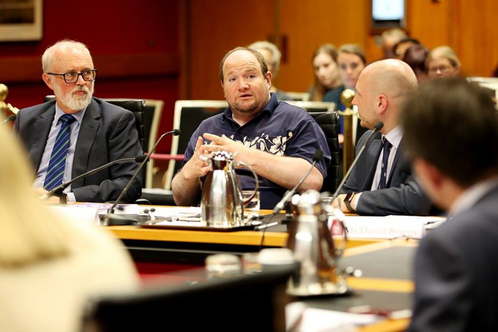 Jim Simpson, Anthony Mulholland, and David Briggs from CID, sitting at a table in the NSW Parliament. Anthony is speaking to a man in the foreground.