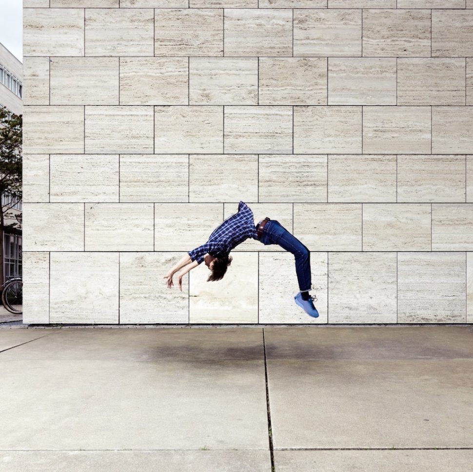 Man doing a backflip in front of a sandstone building.