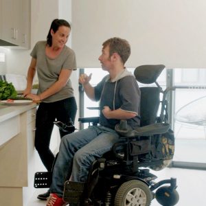 Ben, an electric wheelchair user talking to a young woman in an accessible kitchen
