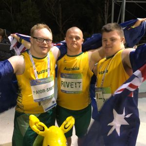 Ben and his friends wearing their team Australia uniforms, Australian flags, and an inflatable kangaroo mascot. They are raising their arms in victory, and look happy and proud.