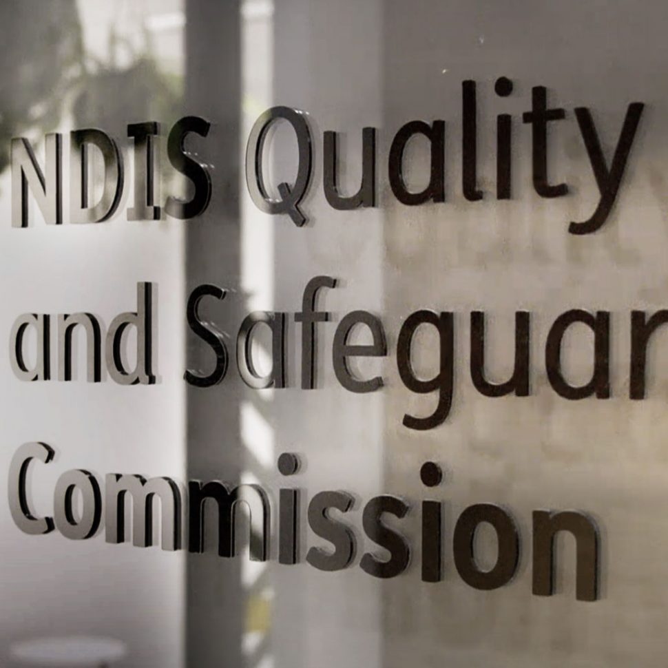 Photo of a glass panel with a section of the NDIS Quality and Safeguards Commission logo.
