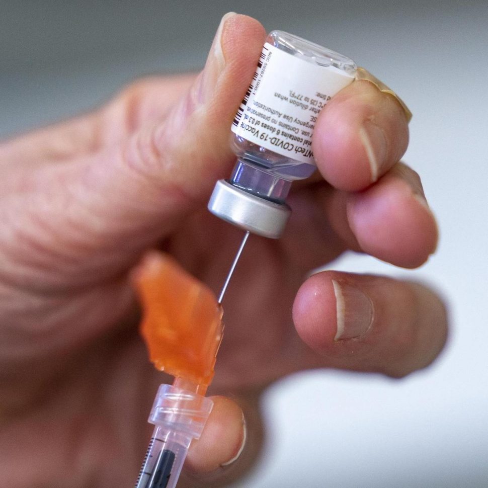 Close up of a needle taking a dose of a COVID vaccine from a small vial.