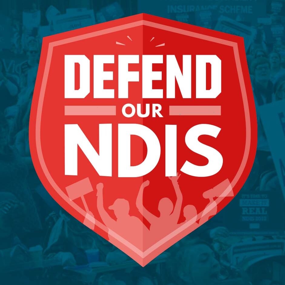 Defend our NDIS written in a shield. People are rallying in the background.