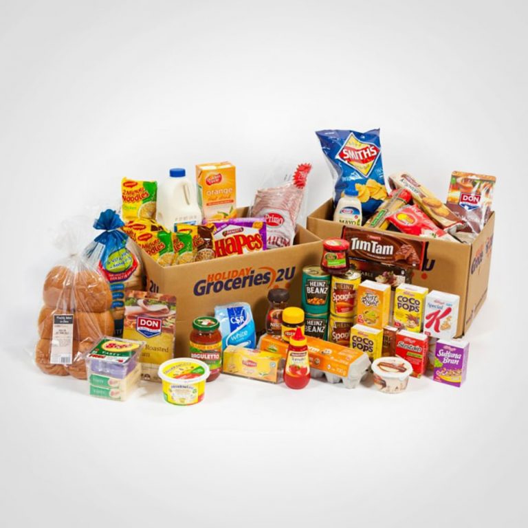 Picture of some groceries laid out on a table. Some of the groceries are in a box while others are sitting beside it. It includes things like chips, bread rolls and Tim Tams. Because everyone knows Tim Tams are essential in a crisis