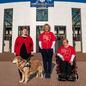 Leah, our Chair and her guide dog Lisa, Kirsten, our Campaign Director, and Lynne, an EAC Champion all wearing red EAC teeshirts out the front of Parliament House