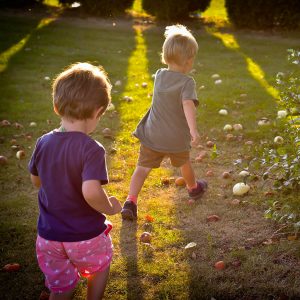 Photo of two young children running away from the camera outside in the grass.