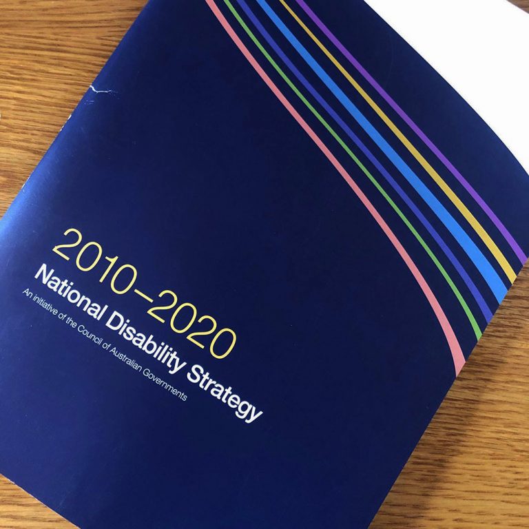 A photo of the National Disability Strategy. It has a blue and white cover with six ribbons of colour flowing across the front. The title reads "2010 - 2020 National Disability Strategy An initiative of the Council of Australian Governments"
