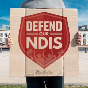 Person holding a "Defend Our NDIS" sign up outside Parliament House