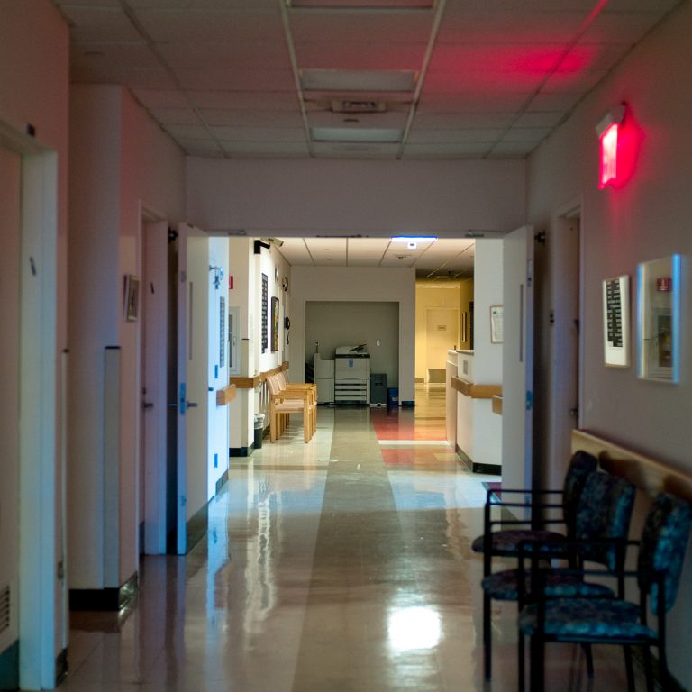 photo of the inside of a nursing home corridor at night. A photocopier is down the end, and some chairs are in the hall.