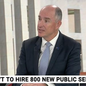 Screenshot from a TV news interview showing NDIS Minister Stuart Robert speaking in front of a Parliament House background. The ticker tape below says "... to hire 800 new public..."