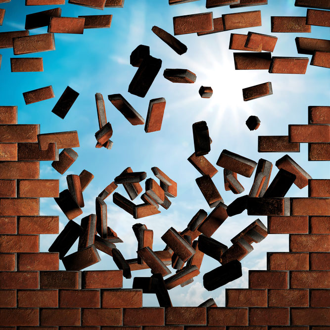 A brick wall mid-demolition revealing a sunny and bright blue sky behind it.